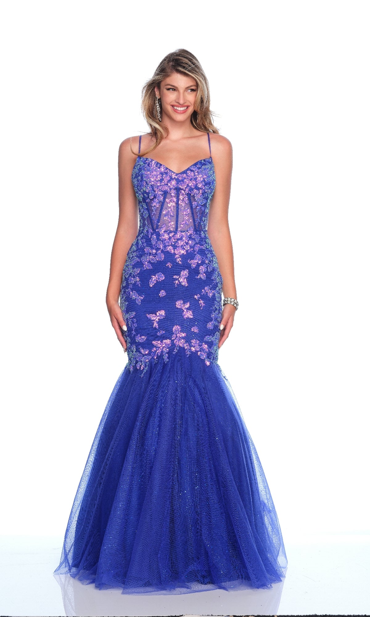 A woman poses in the Blue Mermaid Prom Dress: Dave & Johnny 12134, featuring royal blue glitter fabric, pink sequin embellishments, thin straps, and a tulle skirt against a plain white background.